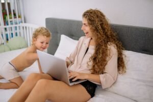 A mother and child engaging with a laptop on bed, showcasing family joy.